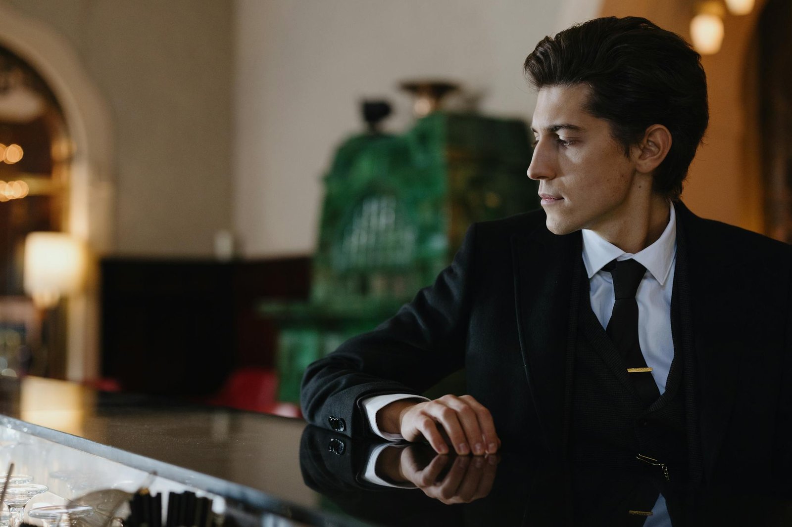 Elegantly dressed man in a suit at a stylish bar with reflective counter. Retro sophistication indoors.
